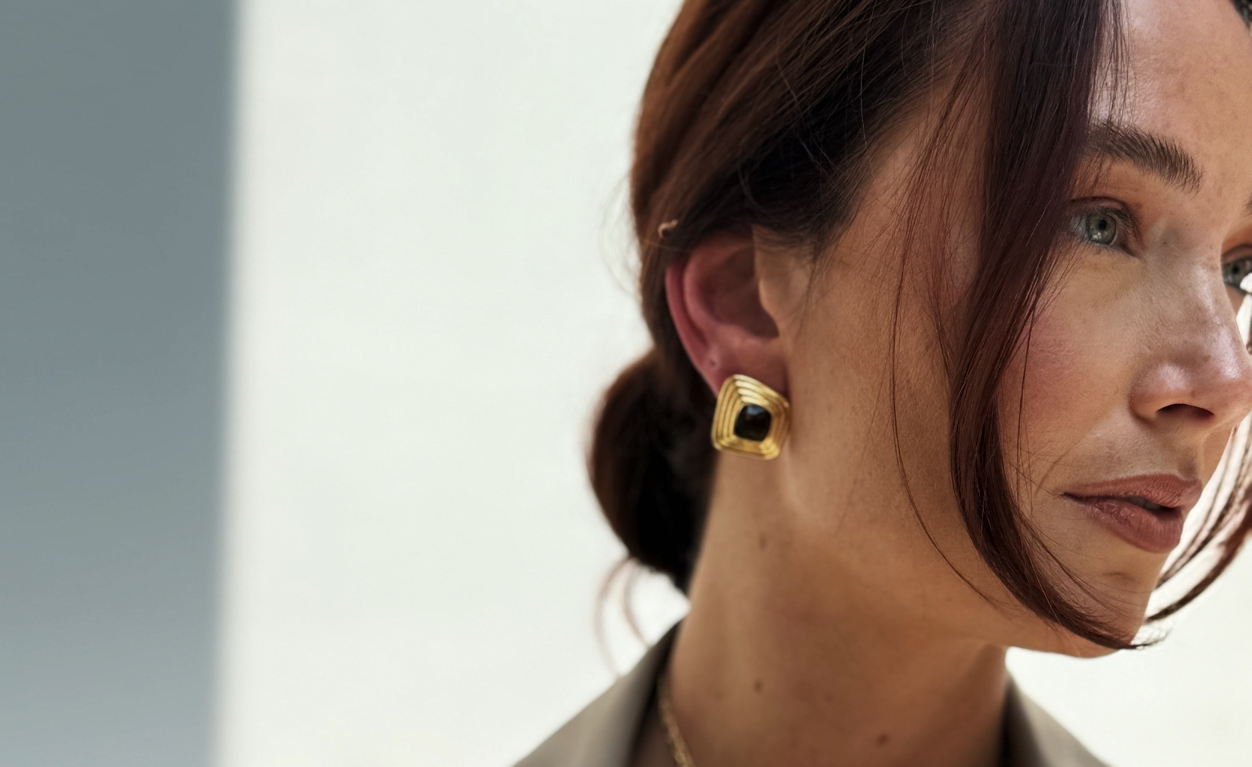 Woman wearing a beige trench coat with a necklace and earrings against a light background